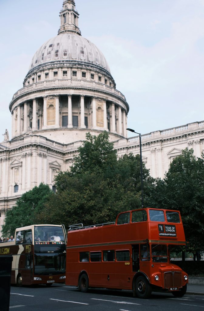 A red double decker bus driving past a tall building